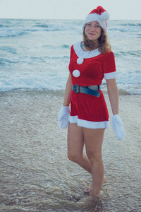 穿着圣诞老人的女孩站在海滩或海洋上。 圣诞节之旅的概念。 新年快乐，圣诞快乐