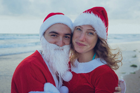 幸福的一对夫妇穿着圣诞老人的服装在海滩上散步。 圣诞节假期的概念。