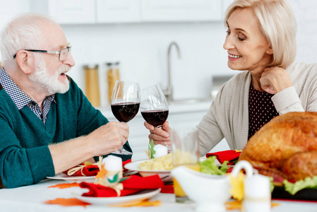 微笑的老夫妇在餐桌上喝着酒杯和烤火鸡亲密接触