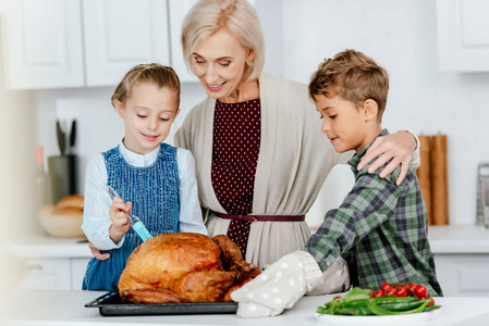 可爱的兄弟姐妹在厨房和祖母一起准备感恩节火鸡