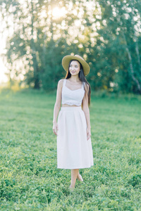 穿着帽子和夏装在田野上散步的女孩。 在森林和大自然中微笑和笑着美丽的日落。 白色连衣裙和黑麦倾斜的田野。 快乐的旅行者生活方式。