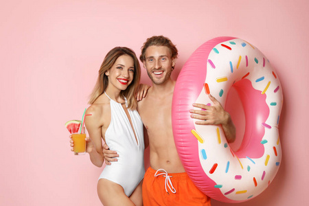 快乐的年轻夫妇，带充气戒指和彩色背景的鸡尾酒的海滩服装