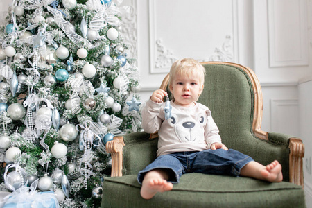 肖像小男孩。新年快乐。装饰圣诞树。圣诞节早晨在明亮的客厅里。坐在绿色的椅子上