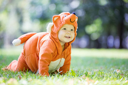 穿着狐狸服装在公园草坪上爬行的可爱微笑女婴