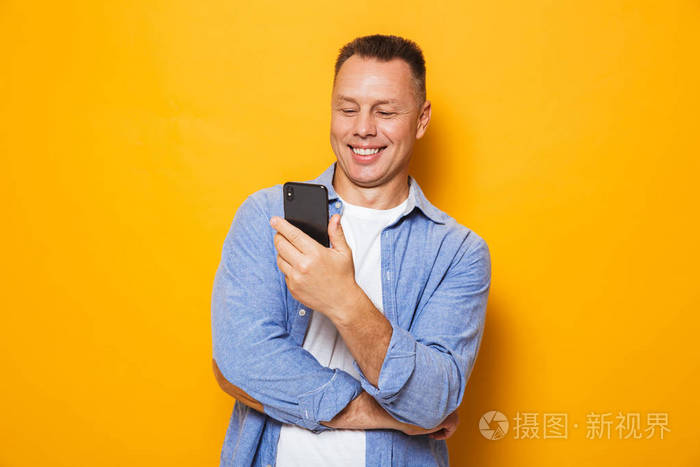 一个快乐的中年男人在黄色背景下看手机的画像照片 正版商用图片12re0u 摄图新视界