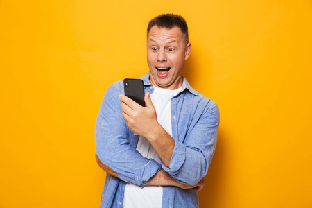 一位兴奋的中年男子在黄色背景下看手机的画像
