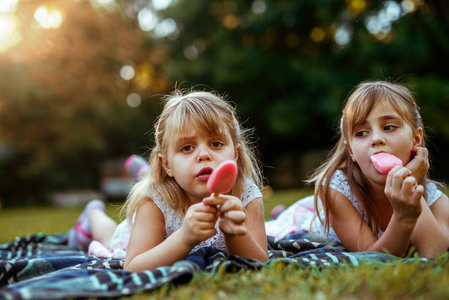 特写两个金发女孩在野餐时喜欢吃冰淇淋的照片。