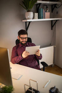 一位微笑的年轻商人在家里使用数字平板电脑的肖像。