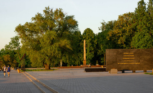 方尖碑K.米宁和波扎斯基永恒的火焰和纪念墙在日落在尼兹尼诺夫哥罗德。 一对牵着手走路的夫妇。 许多绿树被夏日夕阳照亮。
