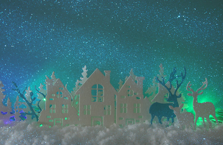 神奇的圣诞纸剪下冬天的背景景观，房子树，鹿和雪在北极光的背景下