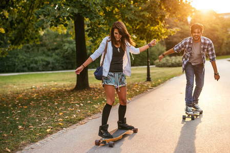 日落时一对年轻夫妇在路上驾驶滑板的照片。