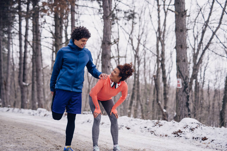 一对合适的夫妇在冬天锻炼时在树林里伸展的肖像。