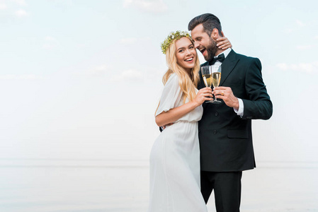 快乐的新郎和新娘在海滩上用香槟酒杯拥抱和亲吻