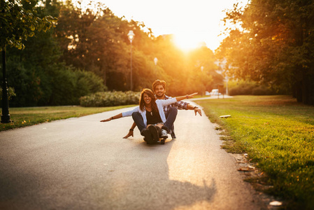 一对快乐微笑的年轻夫妇在日落时在街上玩滑板的照片。