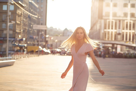 漂亮的金发模特在阳光下的街道上摆着飘扬的头发。 女性时尚概念。 空的空间