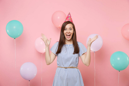 迷人的年轻快乐女人的肖像,戴着生日帽和蓝色连衣裙,双手在明亮的粉红