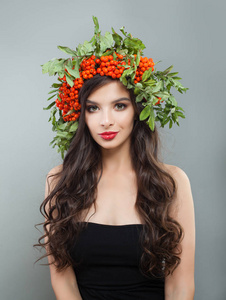 深色女士时装模特，有健康的卷发妆和红色浆果和绿叶。