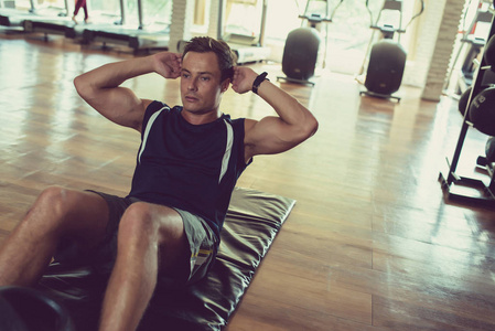 穿着运动服的英俊肌肉男躺在垫子上做腹部运动照片