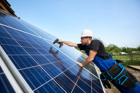 技术人员安装太阳能电池板的简介使用电气螺丝刀在蓝天复制空间背景。 独立的外部太阳能系统安装效率和专业理念。