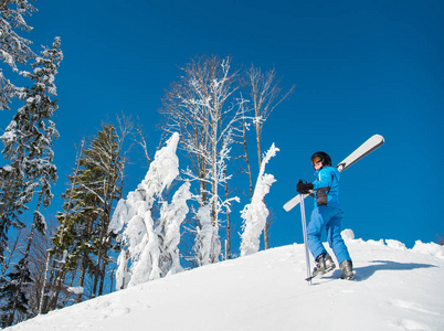拍摄了一名女子滑雪者，欣赏着美丽的雪山景色，同时走上斜坡，扛着她的滑雪板，肩上交叉空间，冬季自由下坡，极端。
