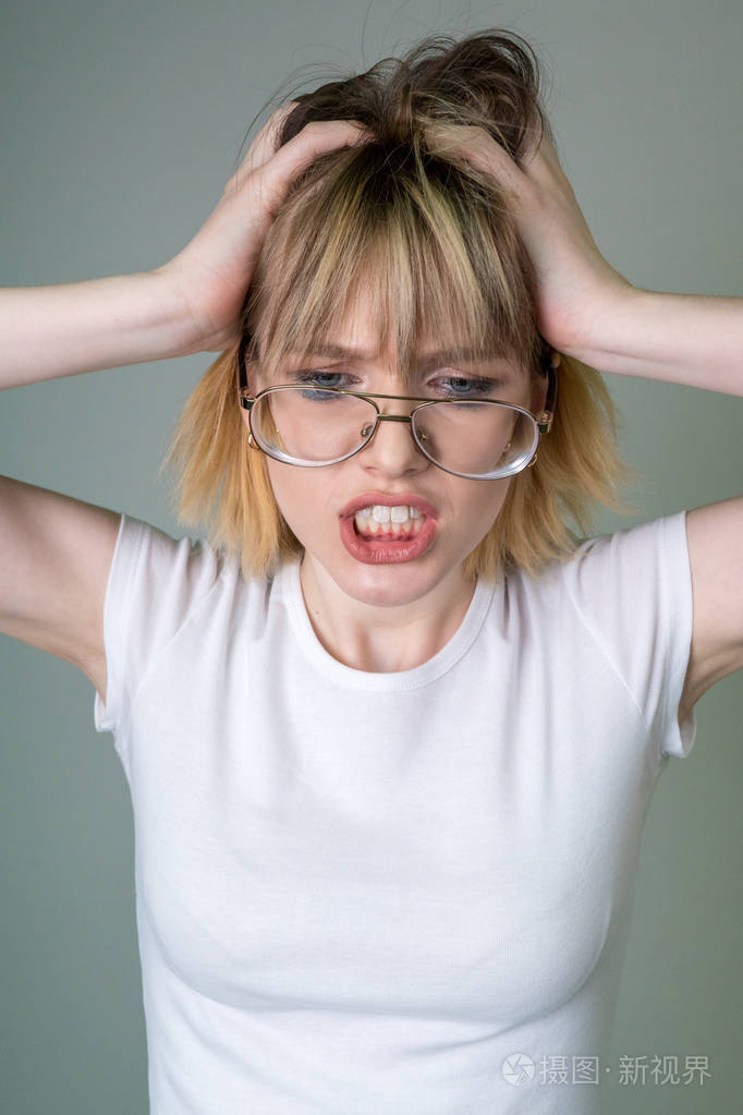 情绪紧张的女孩与金发在透明眼镜, 握在头上, 使鬼脸