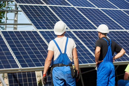 背面视图的两名工人站在高外部太阳能电池板照片Voltaic系统安装在钢平台上。 可再生生态绿色能源生产理念。