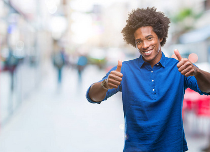 美国黑人男子在孤立的背景下赞成做积极的手势，用手竖起大拇指，微笑，为成功而高兴。 看着相机赢家的手势。