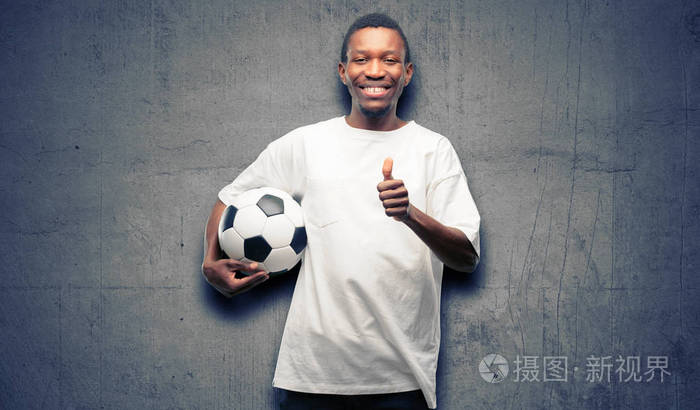 非洲黑人男子手持足球笑容满面竖起大拇指手势对着镜头表示喜欢和赞同