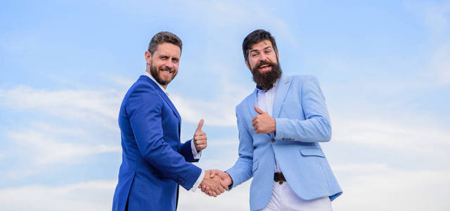 业务合作伙伴确认交易交易。男子正式西装握手蓝天背景。企业家握手象征成功成交。两个合伙人认可的商业协议