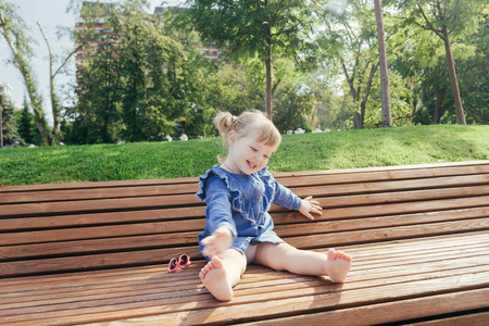 小女孩坐在长凳上，在一个温暖的晴天在城市公园里笑