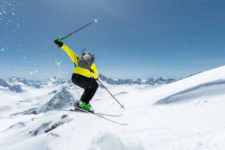一个滑雪运动员在充分的体育设备跳入深渊从山顶在蓝色天空和高加索雪山的背景下从冰川的顶部。从后面查看。Elbrus 地区