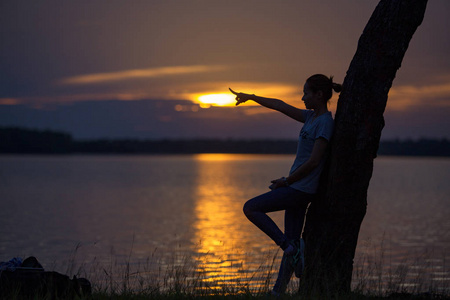 独自一个女孩站着，手指针在河边的剪影日落上。
