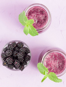 黑莓冰沙生有机饮料与新鲜成熟的森林浆果在粉紫背景。 素食甜维他命生态饮料的顶部视图健康饮食概念。