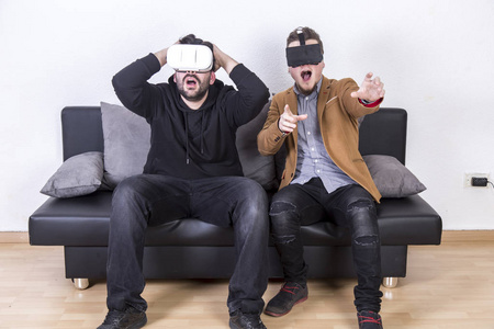 两个吃惊的男人张开嘴，戴着虚拟现实眼镜，坐在房间的沙发上