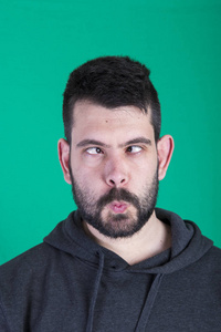 深色头发的男人,眯着眼睛在绿色背景的工作室里摆姿势照片