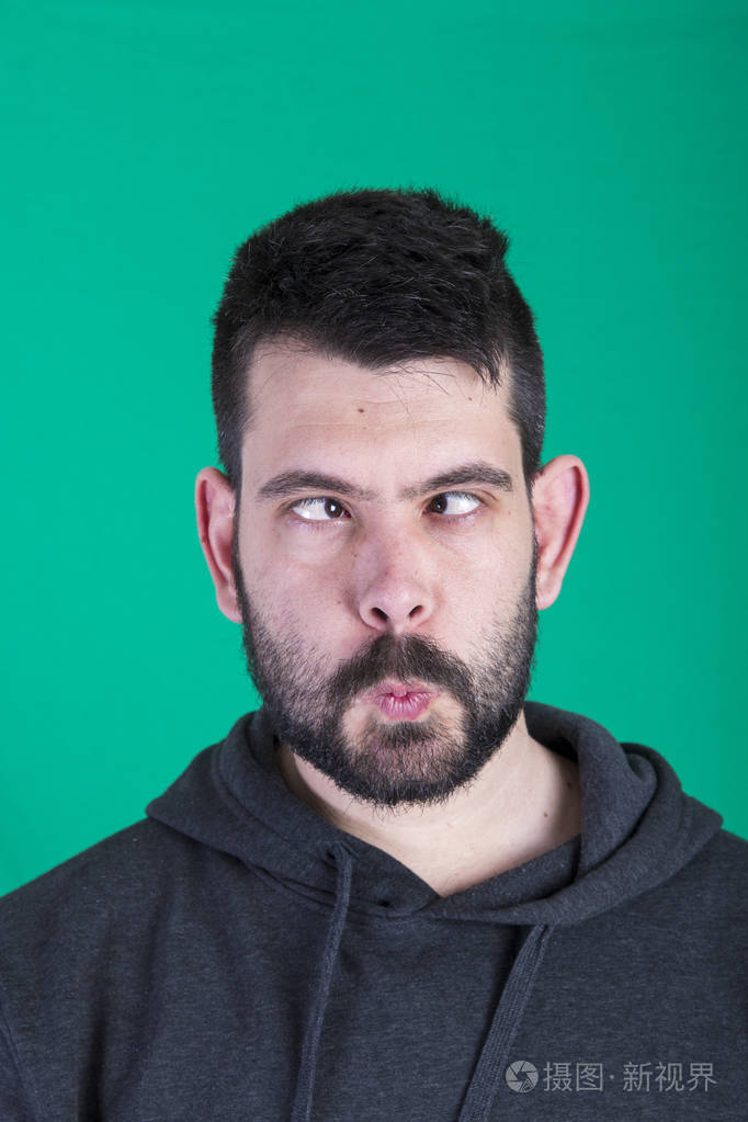 深色头发的男人眯着眼睛在绿色背景的工作室里摆姿势