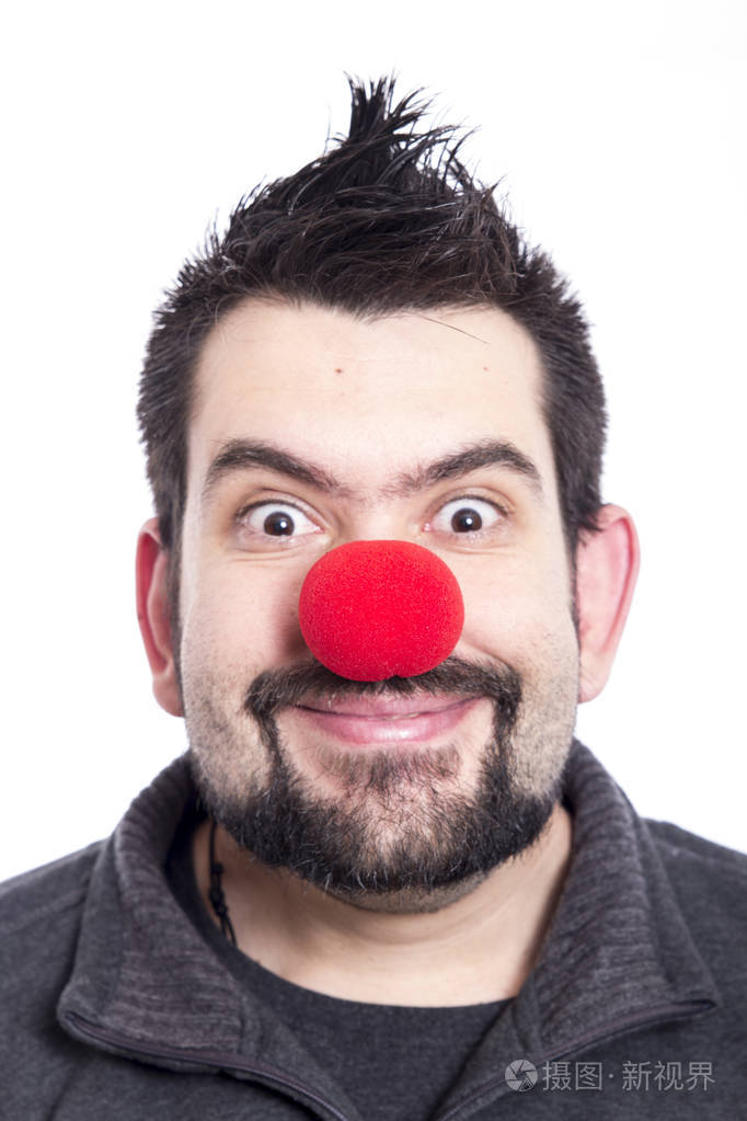 带着红色小丑鼻子的微笑男人在演播室摆姿势看着摄像机