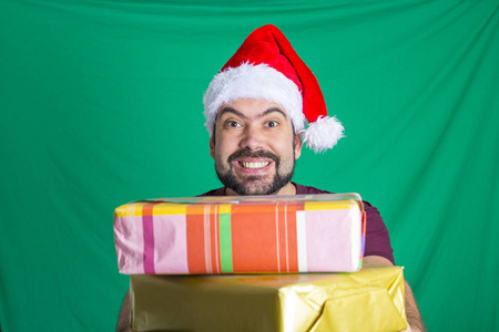 戴着红色圣诞老人帽的大胡子男人看着相机，拿着礼品盒