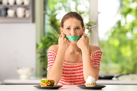 情绪化的女人嘴上有测量带，厨房里有不健康的食物。饮食概念