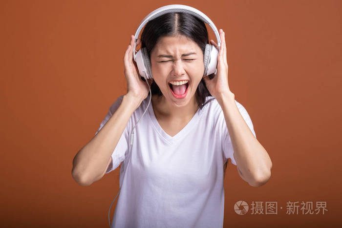 年轻的亚洲女人听音乐时带着头电话,心情很兴奋 时尚生活方式概念