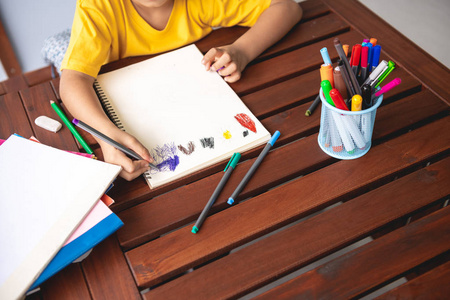 孩子们的家庭作业。 年轻的混血男孩在家的露台上做作业。 绘图着色。 集中精神。 回到学校的概念。