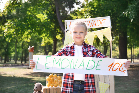 在公园的柠檬水摊附近拿着价格横幅的小女孩