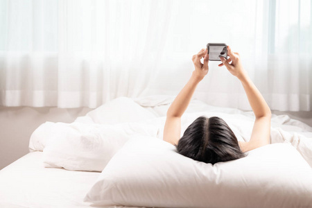 女人在床上浏览电话。 亚洲女人在白色顶部使用电话快乐的心情。 现代生活观念。