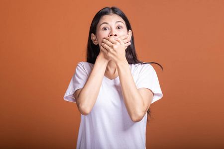 年轻的亚洲时髦女人穿着白色t恤,姿势震惊,双手捂住嘴.