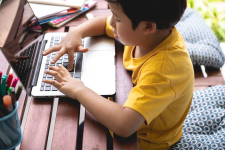 孩子们的家庭作业。 年轻的混血男孩在家里的露台上用笔记本电脑做作业。 集中情绪接近。 回到学校的概念。