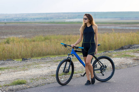 女孩骑着山地车在越野上，美丽的肖像自行车在日落健身女孩骑着现代碳纤维山地自行车。