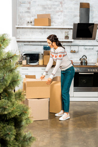在新家搬迁期间，妇女与圣诞树一起站在厨房纸板箱附近的选择性焦点