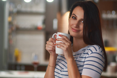 肖像休闲年轻女子在厨房喝茶或咖啡的背景模糊。 近点