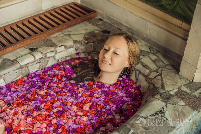 头顶上的妇女正在用热带花卉和芳香油的花瓣洗温泉浴.