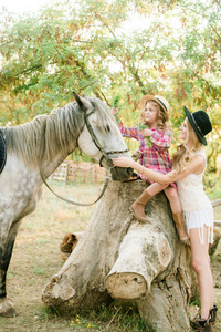 秋天的一天，一个美丽的年轻女孩，金发碧眼，穿着一件绒面夹克，带着条纹，妹妹戴着草帽，穿着一件格子的复古连衣裙，骑着一匹马在乡下